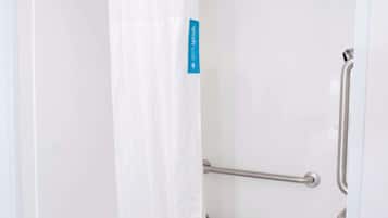 A white bathtub with a shower curtain and grab bars.