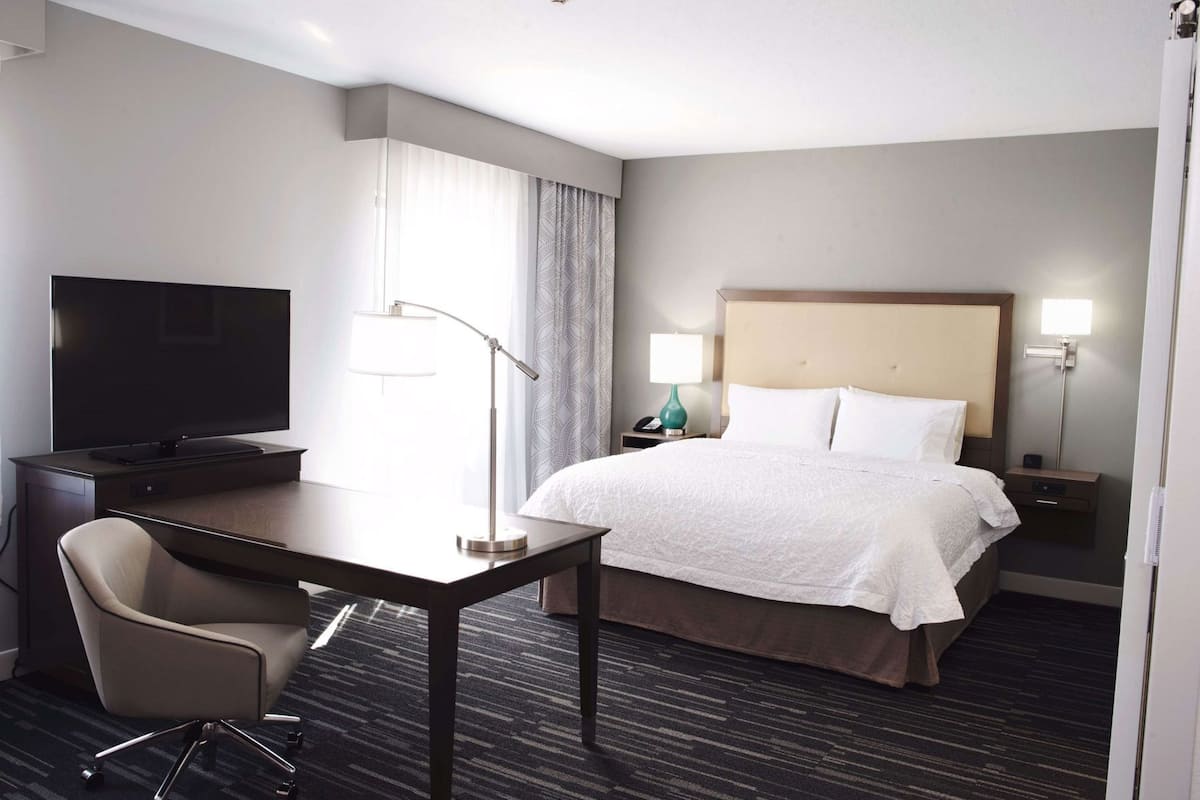 Habitación de hotel con cama, escritorio con silla, televisor y dos lámparas de noche.