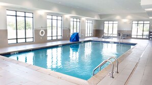 An indoor swimming pool with clear water, tiled floor, and large windows.
