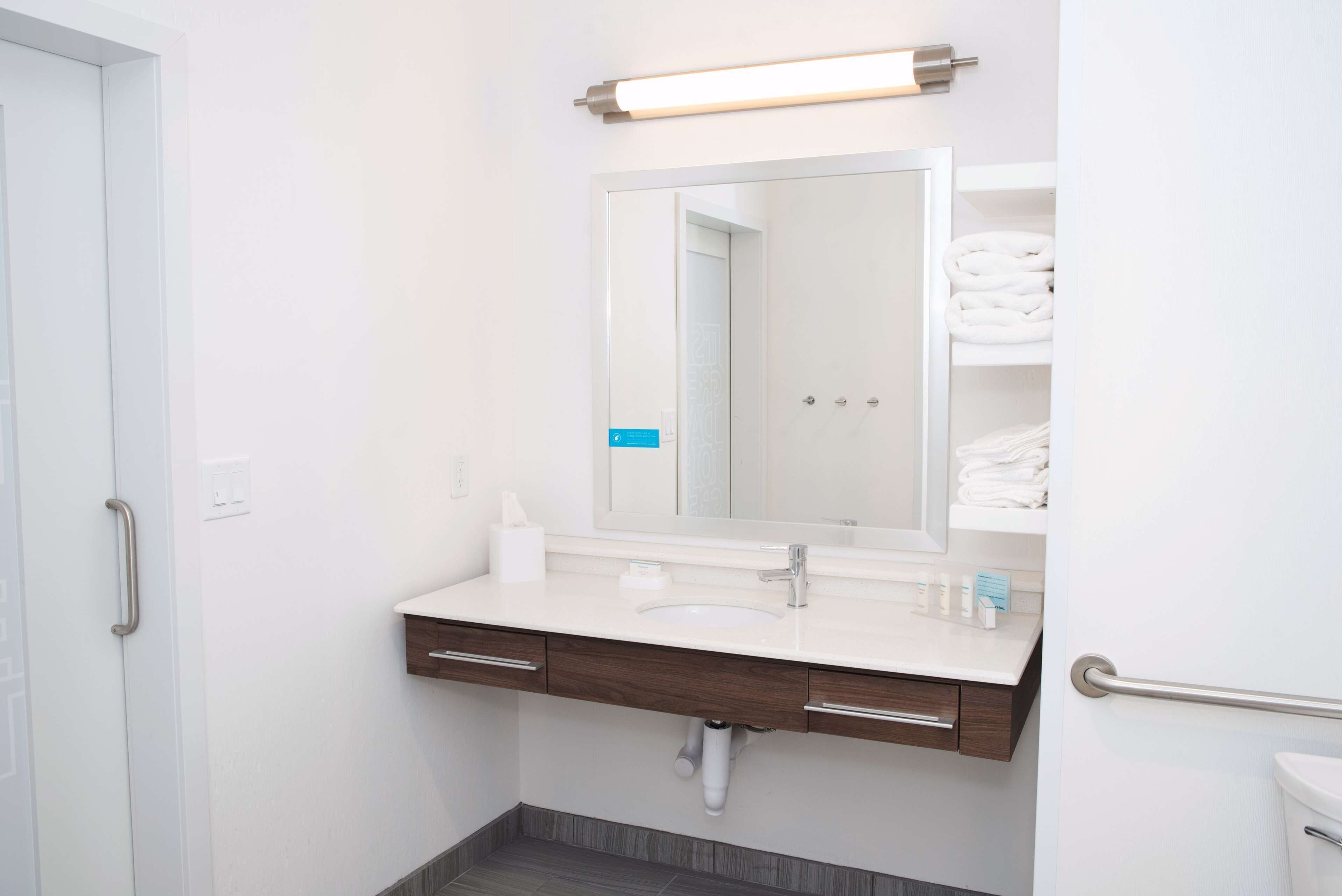 A modern bathroom with a white sink, a large mirror, and a towel rack with folded towels.