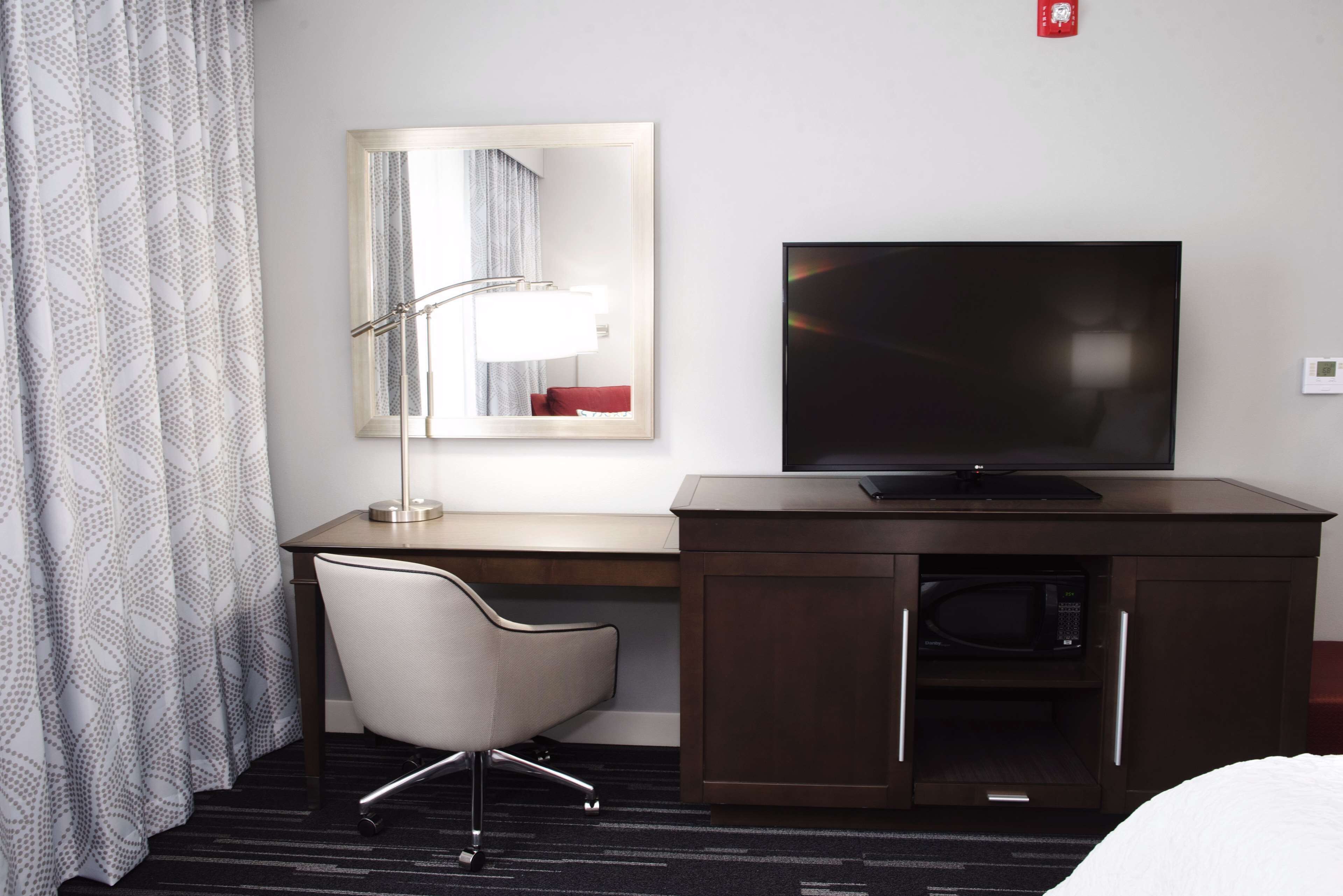 Ein Hotelzimmer mit Schreibtisch, Fernseher, Mikrowelle, Stuhl und einem gemusterten Vorhang.