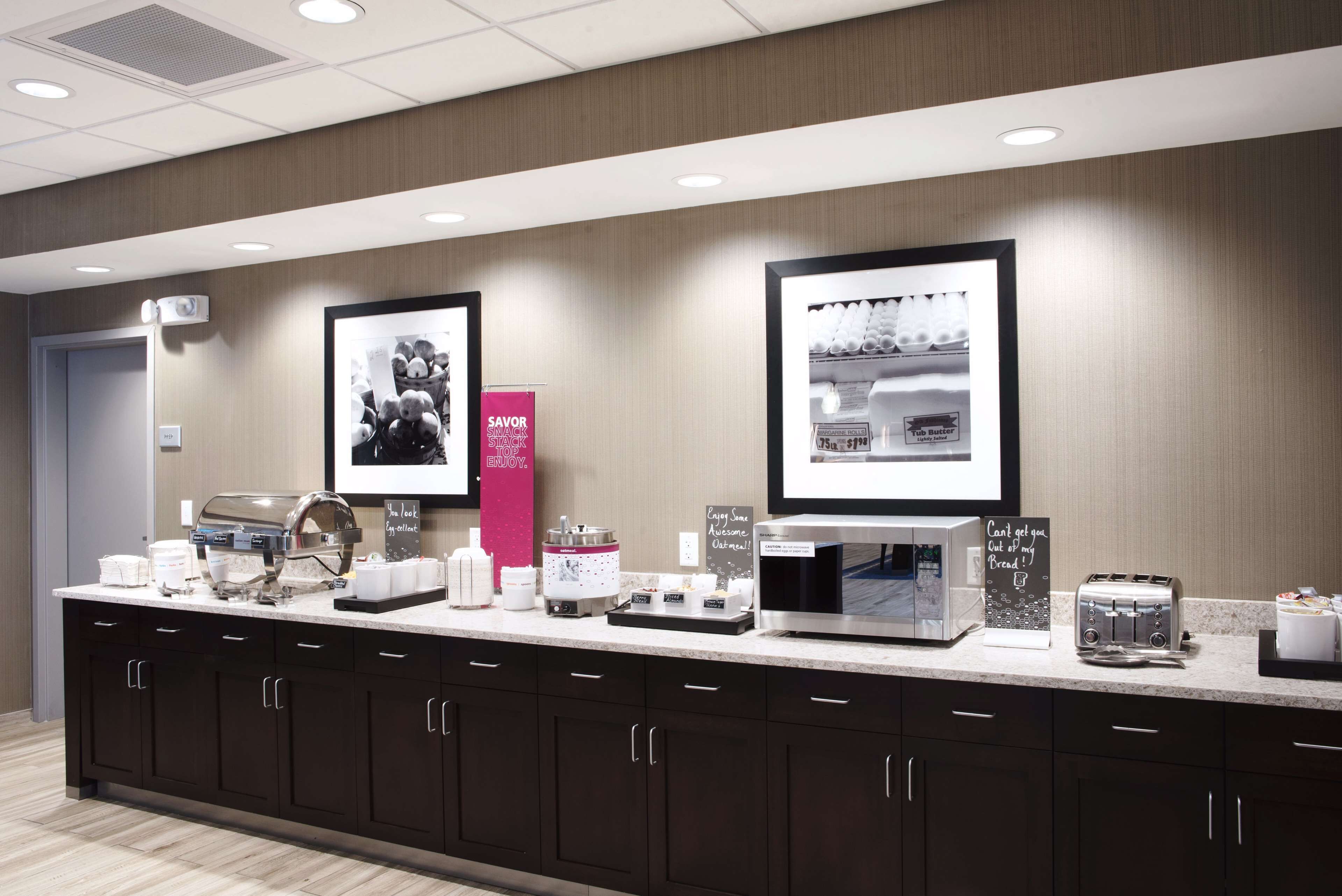 A modern kitchen area with a long counter, various appliances, and framed pictures on the wall.