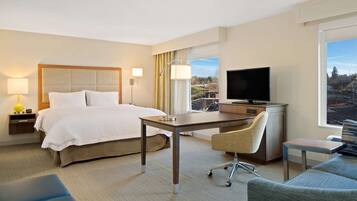 Habitación de hotel con cama, escritorio, silla, televisor y vista a la ciudad.