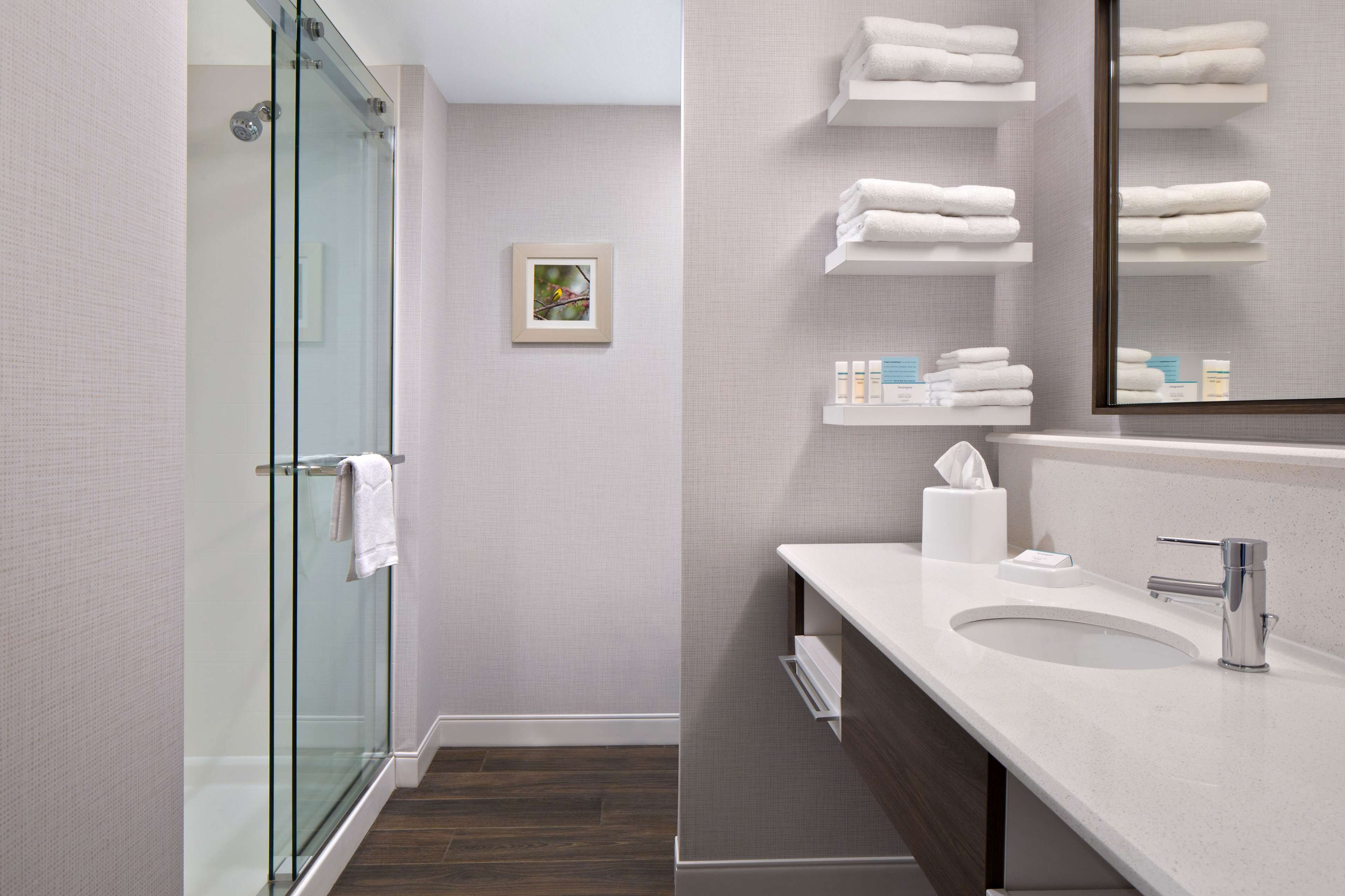 A modern bathroom with a glass shower enclosure, a white sink, and neatly arranged towels on shelves.