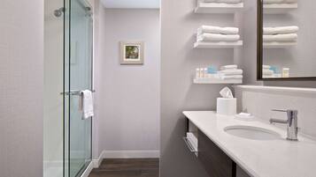 A modern bathroom with a glass shower enclosure, a white sink, and neatly arranged towels on shelves.