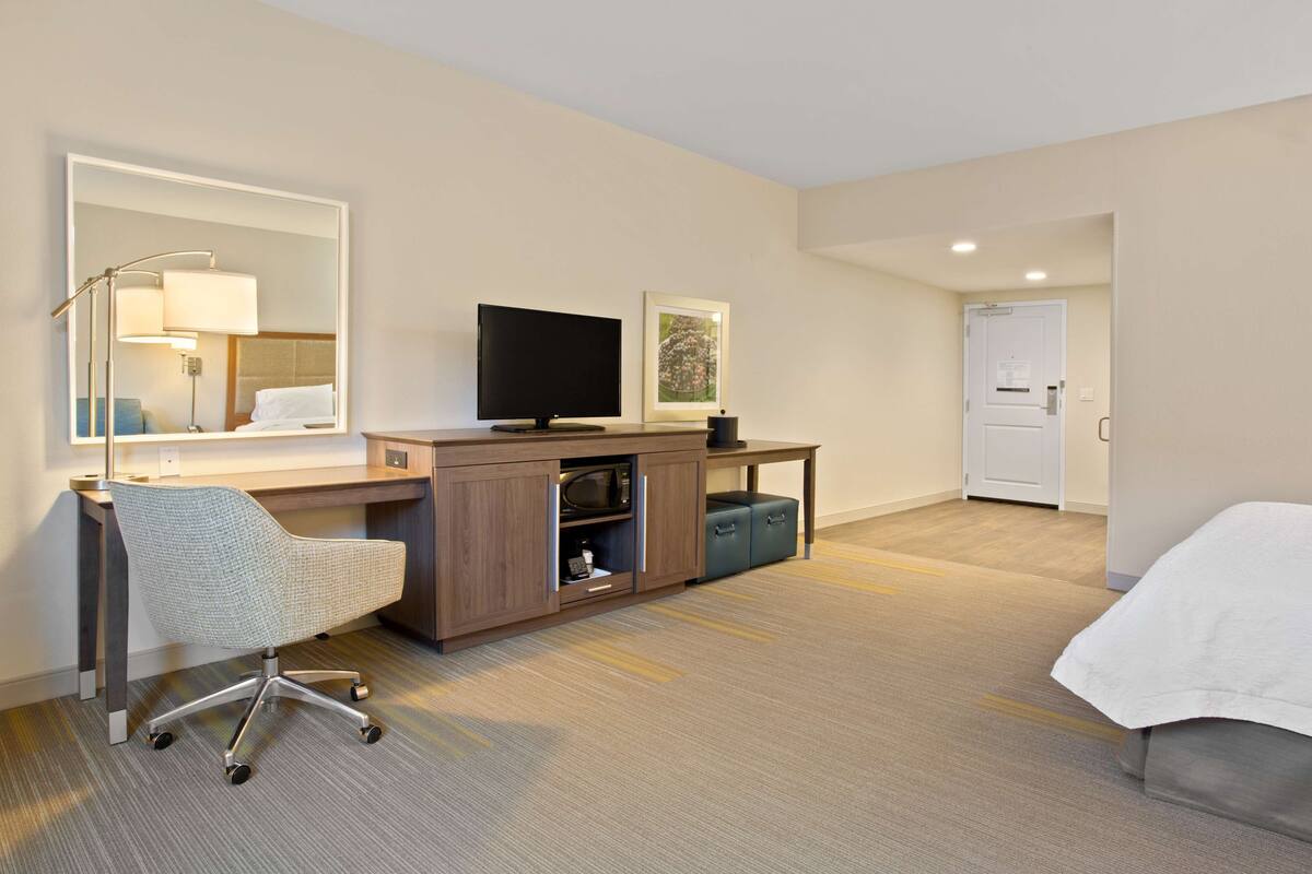 A hotel room with a desk, chair, television, and a bed.