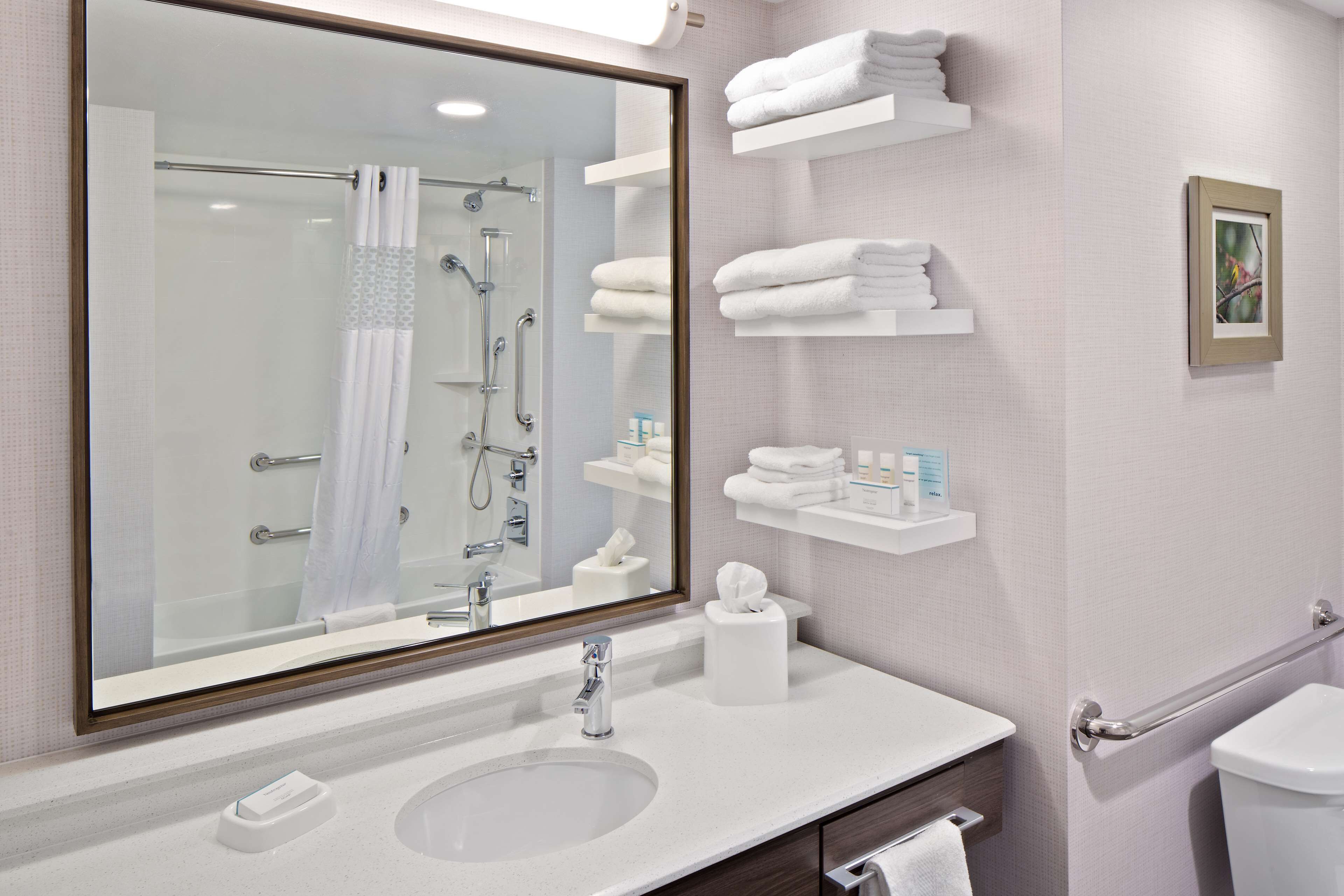 Un baño con un espejo grande, un lavabo, un inodoro y varios estantes con toallas.