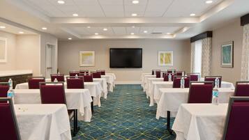 A conference room with rows of tables and chairs, a flat-screen TV, and framed artwork on the walls.