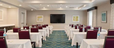 A conference room with rows of tables and chairs, a flat-screen TV, and framed artwork on the walls.