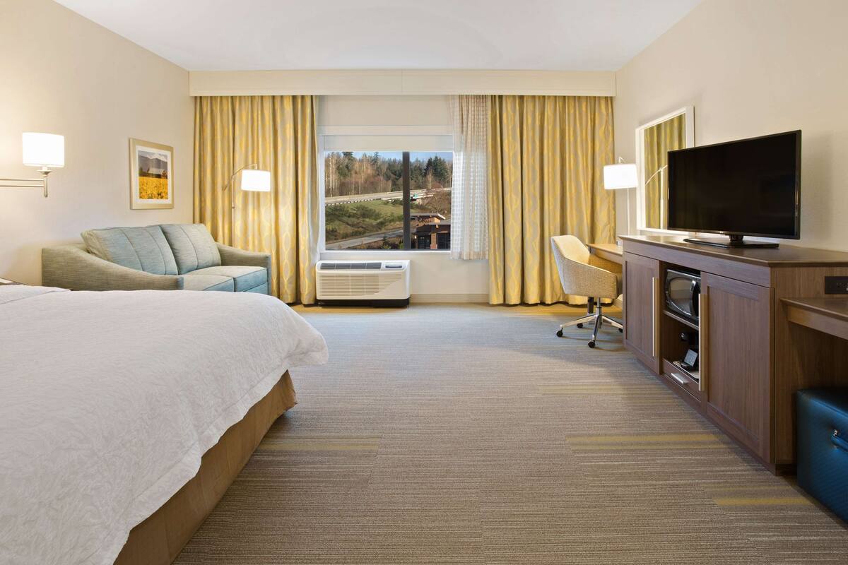A hotel room with a bed, a desk, a television, and a window with curtains.