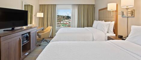 A hotel room with two beds, a TV, a desk, and a view of the city.