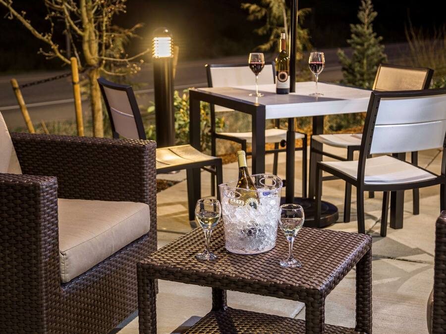 Un área de comedor al aire libre con mobiliario de mimbre, una mesa con una botella de champán y dos copas de vino.