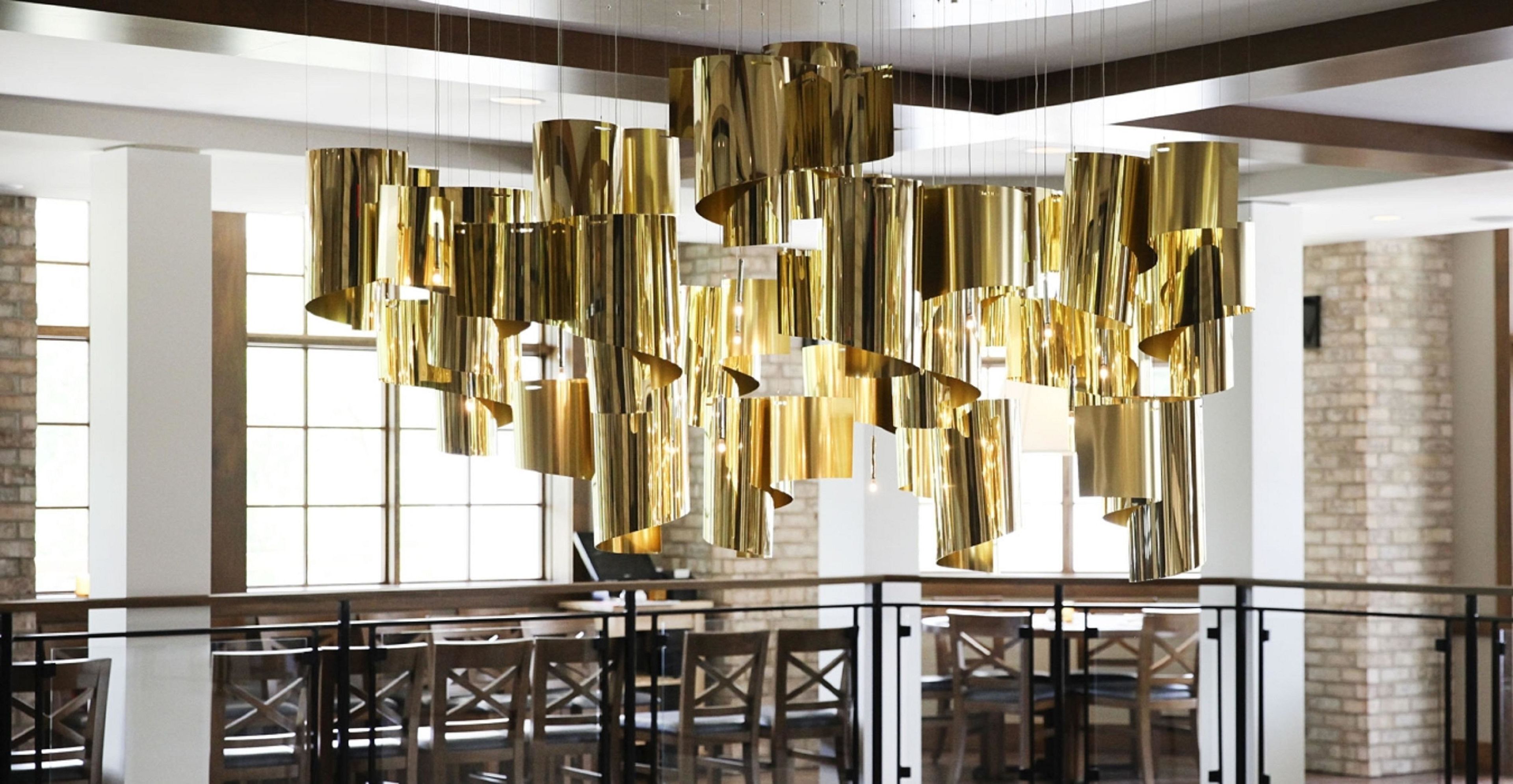 A modern interior with hanging gold fixtures, a staircase, and a brick wall.