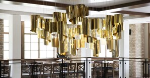 A modern interior with hanging gold fixtures, a staircase, and a brick wall. - The Hotel Landing (Wayzata)