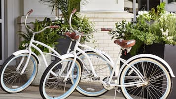 Una bicicleta blanca con aros azules estacionada frente a un edificio de fachada de ladrillo y plantas en macetas.