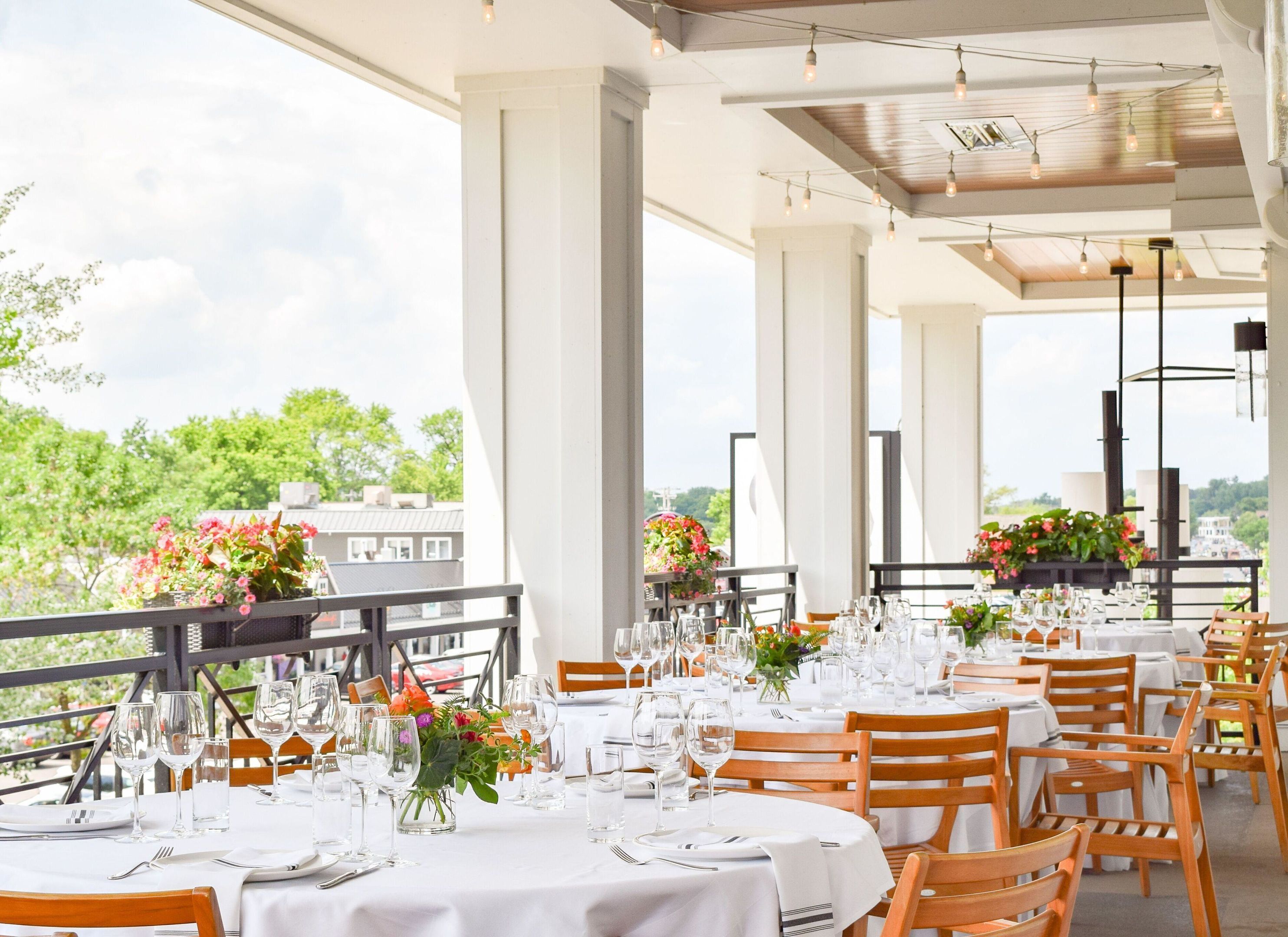An outdoor dining area with tables set for a meal, large windows, and a view of the cityscape.