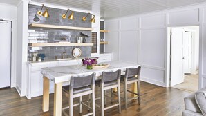 Una cocina moderna con armarios blancos, salpicadero de azulejos grises e iluminación colgante dorada.