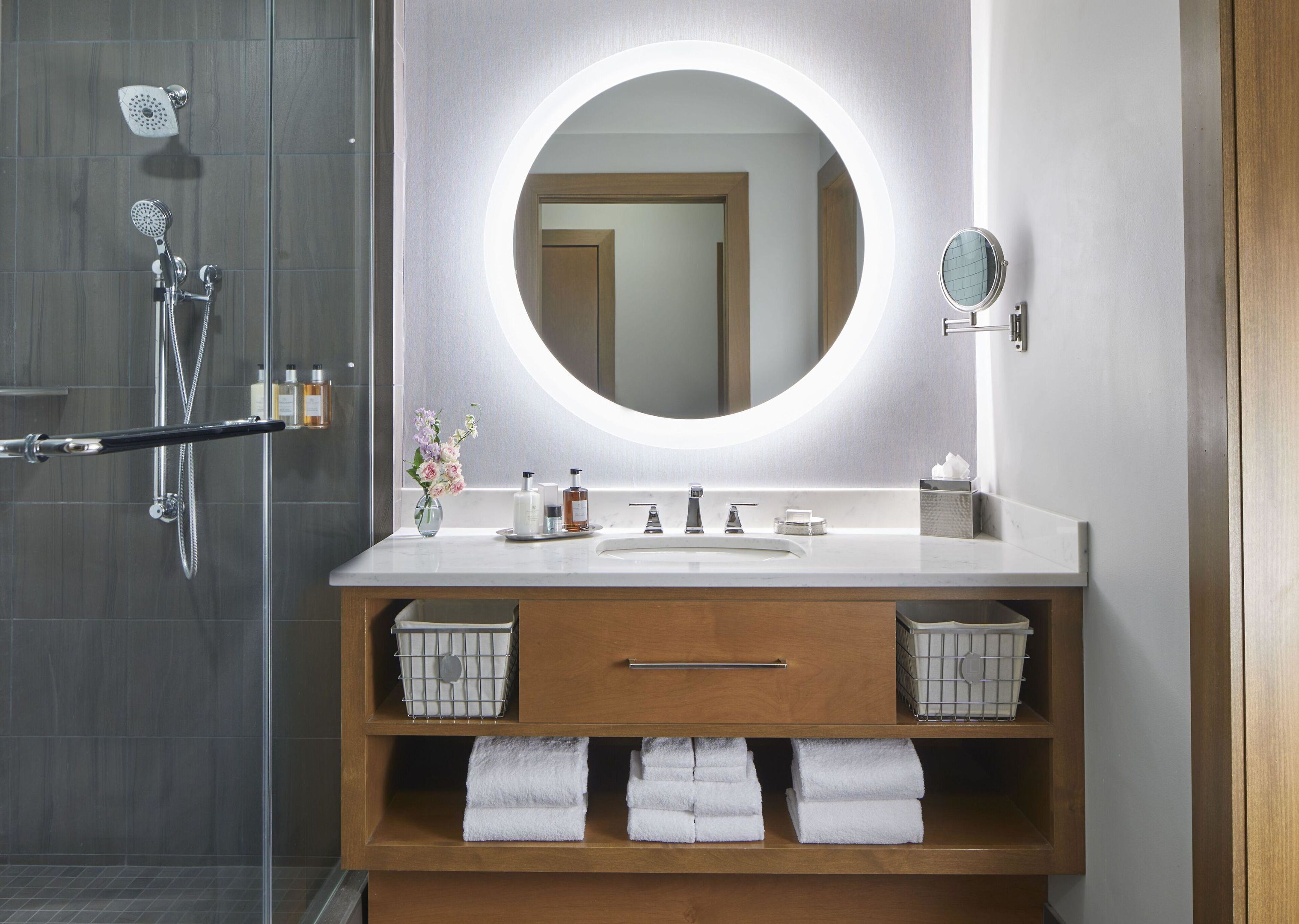 Une salle de bain moderne avec un grand miroir rond, une douche et un meuble-lavabo avec espace de rangement.