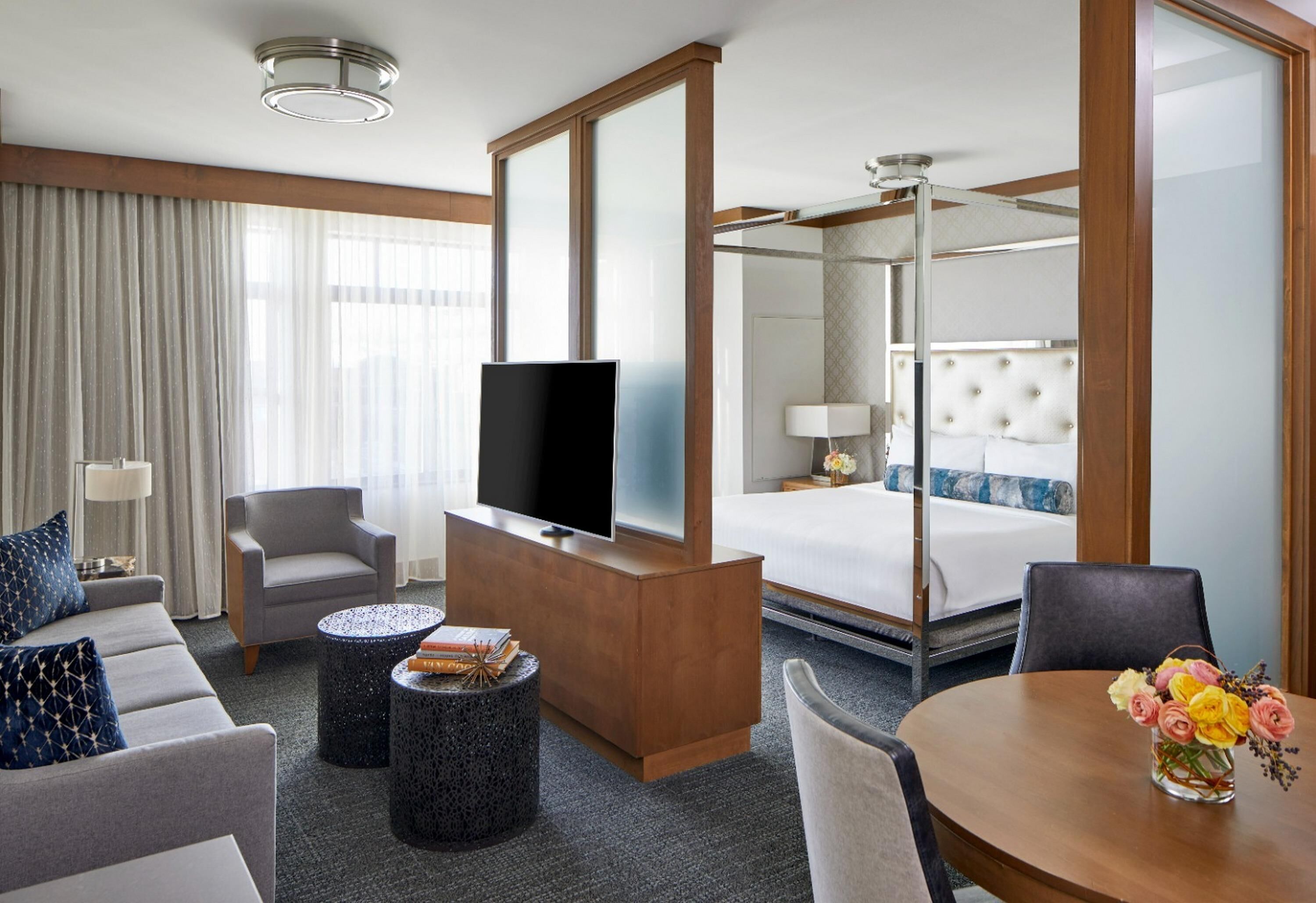 A hotel room with a bed, a TV, a sofa, a coffee table, and a dining table with flowers.