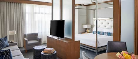 A hotel room with a bed, a TV, a sofa, a coffee table, and a dining table with flowers.