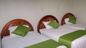 Trois lits simples avec des têtes de lit en bois, du linge de lit blanc et des oreillers verts.
