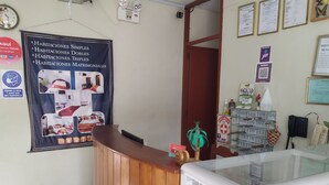 Un espace d’accueil avec un comptoir en bois, une vitrine et une affiche présentant les différents types de chambres.