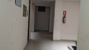 Un couloir avec un ventilateur de plafond, un extincteur et une porte au fond.