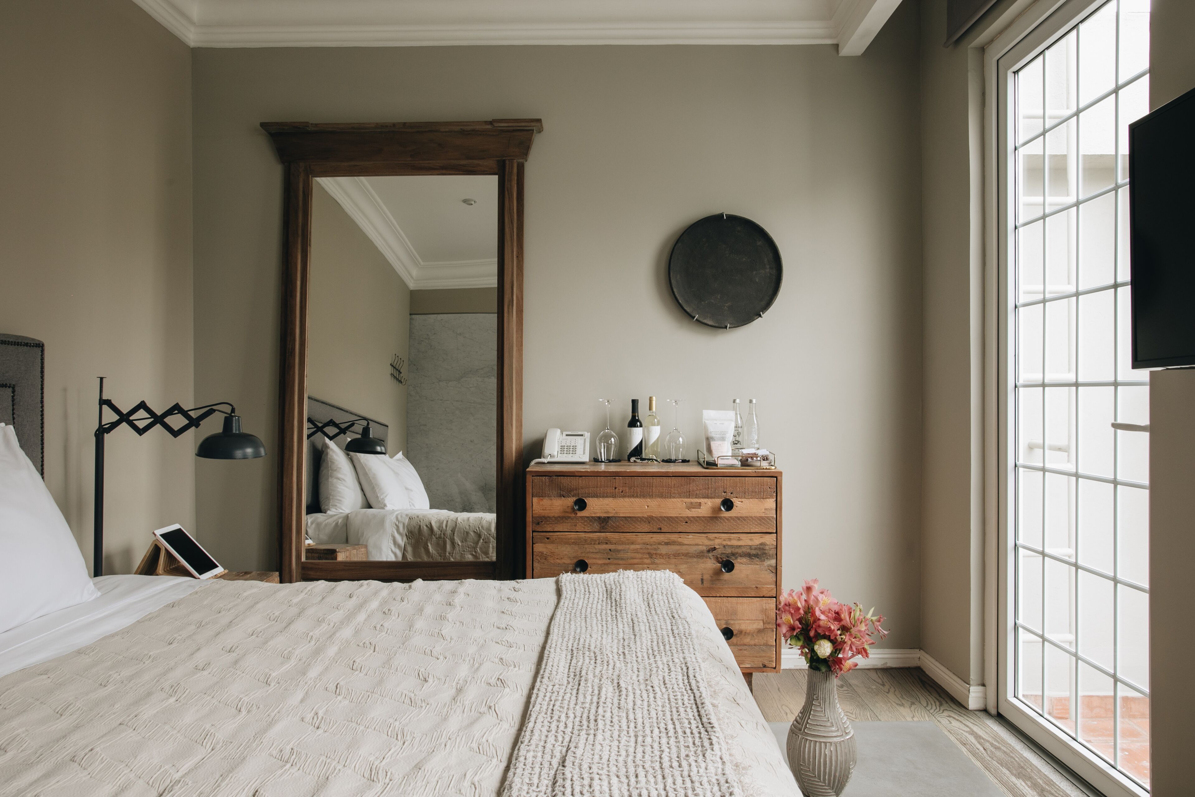 A bedroom with a large bed, a wooden dresser, a mirror, and a window with a view.
