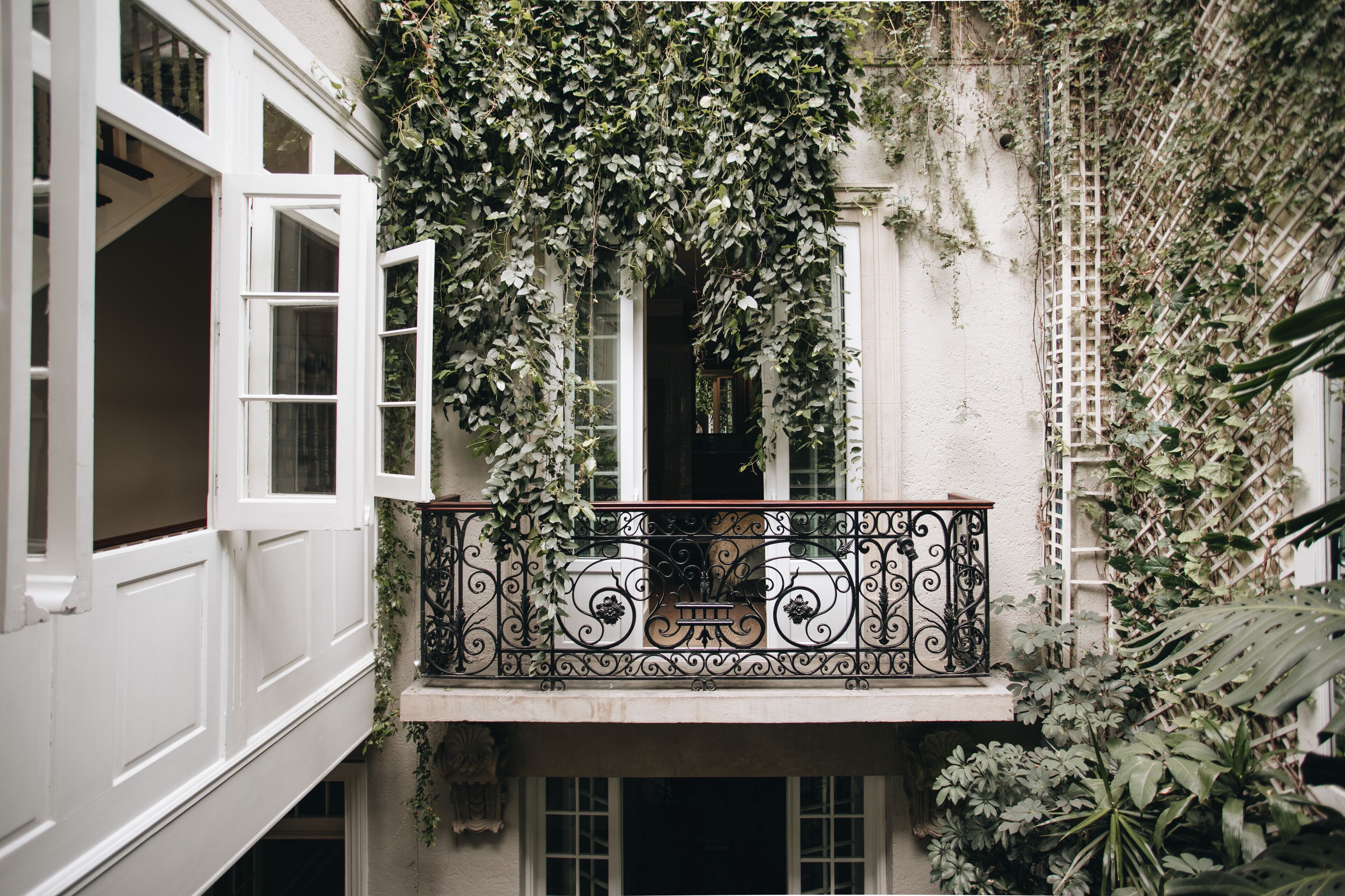 A balcony with ornate wrought iron railings, surrounded by lush greenery and ivy.