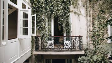 A balcony with ornate wrought iron railings, surrounded by lush greenery and ivy.