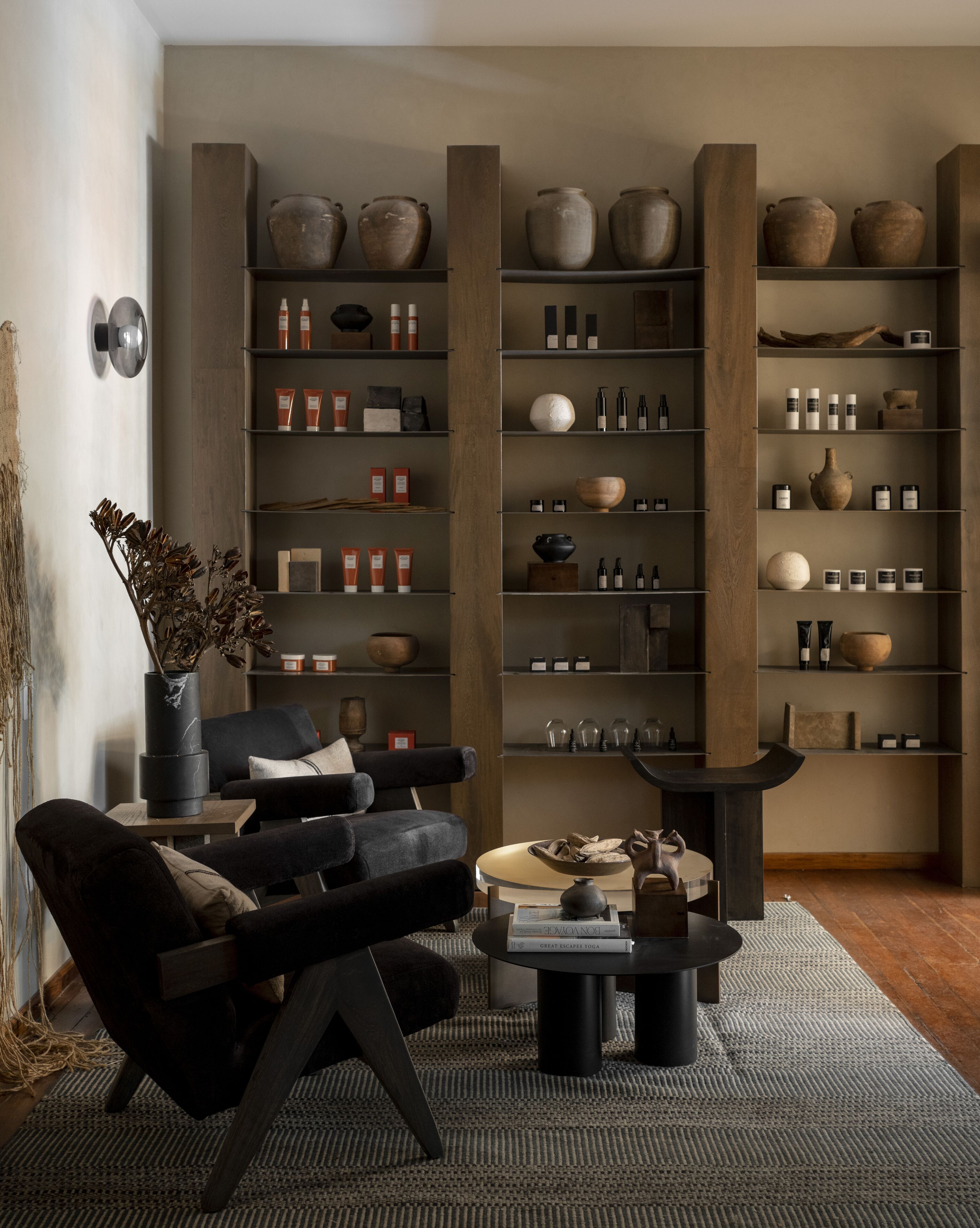 Een moderne woonkamer met een zwarte bank, een salontafel en een boekenkast vol diverse spullen.