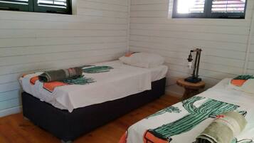 A room with two beds, wooden flooring, and a window with blinds.
