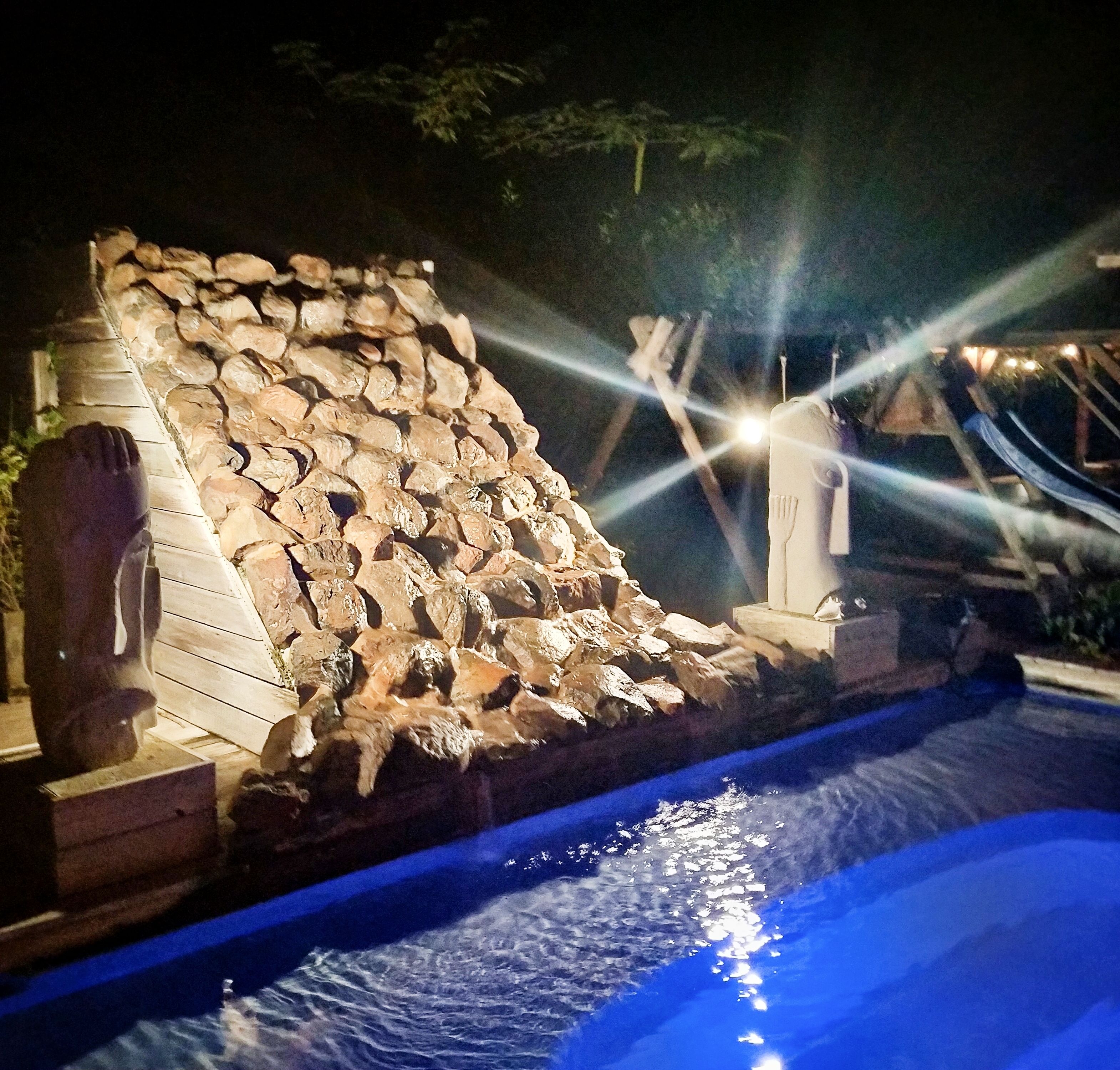 A stone waterfall feature adjacent to a swimming pool.