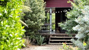 A rustic building with a covered porch, surrounded by dense greenery and a gravel path. - Red Palm Village (Kralendijk)