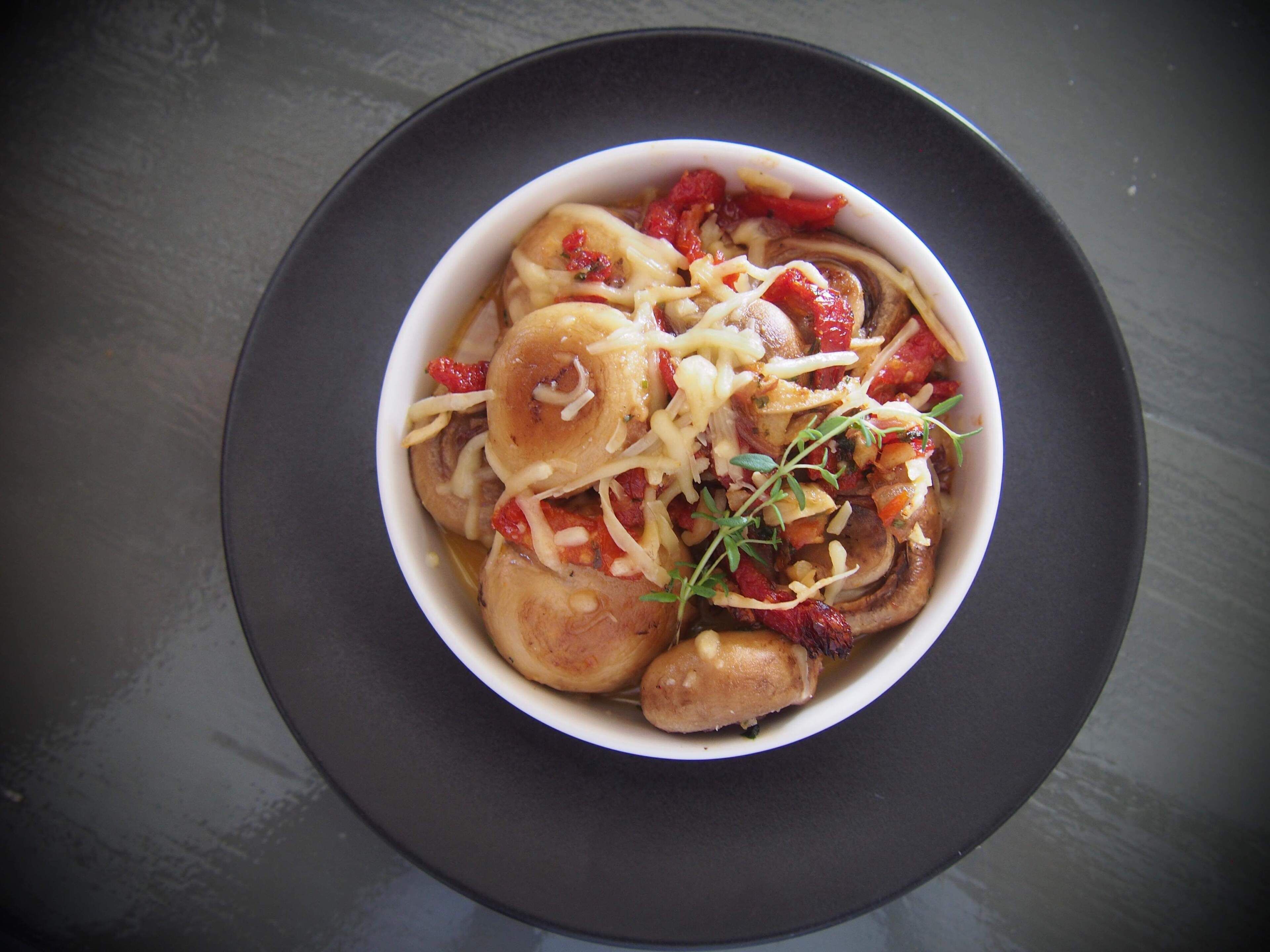 A bowl of food with mushrooms, cheese, and herbs on a dark plate.