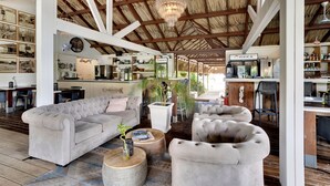 A spacious living area with a high ceiling, a chandelier, and a bar area with a sign reading "OSKA". - Red Palm Village (Kralendijk)