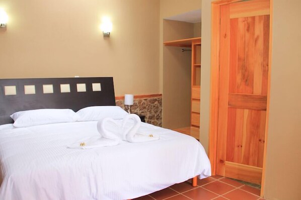 A neatly made bed with white linens and towels, a stone accent wall, and a wooden wardrobe.