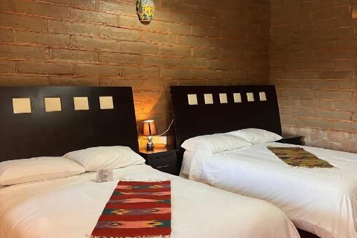 Une chambre avec deux lits, des poutres en bois au plafond et un mur en briques.