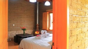 Una habitación acogedora con pared de ladrillo, chimenea, cama con ropa de cama blanca y un jarrón de flores.