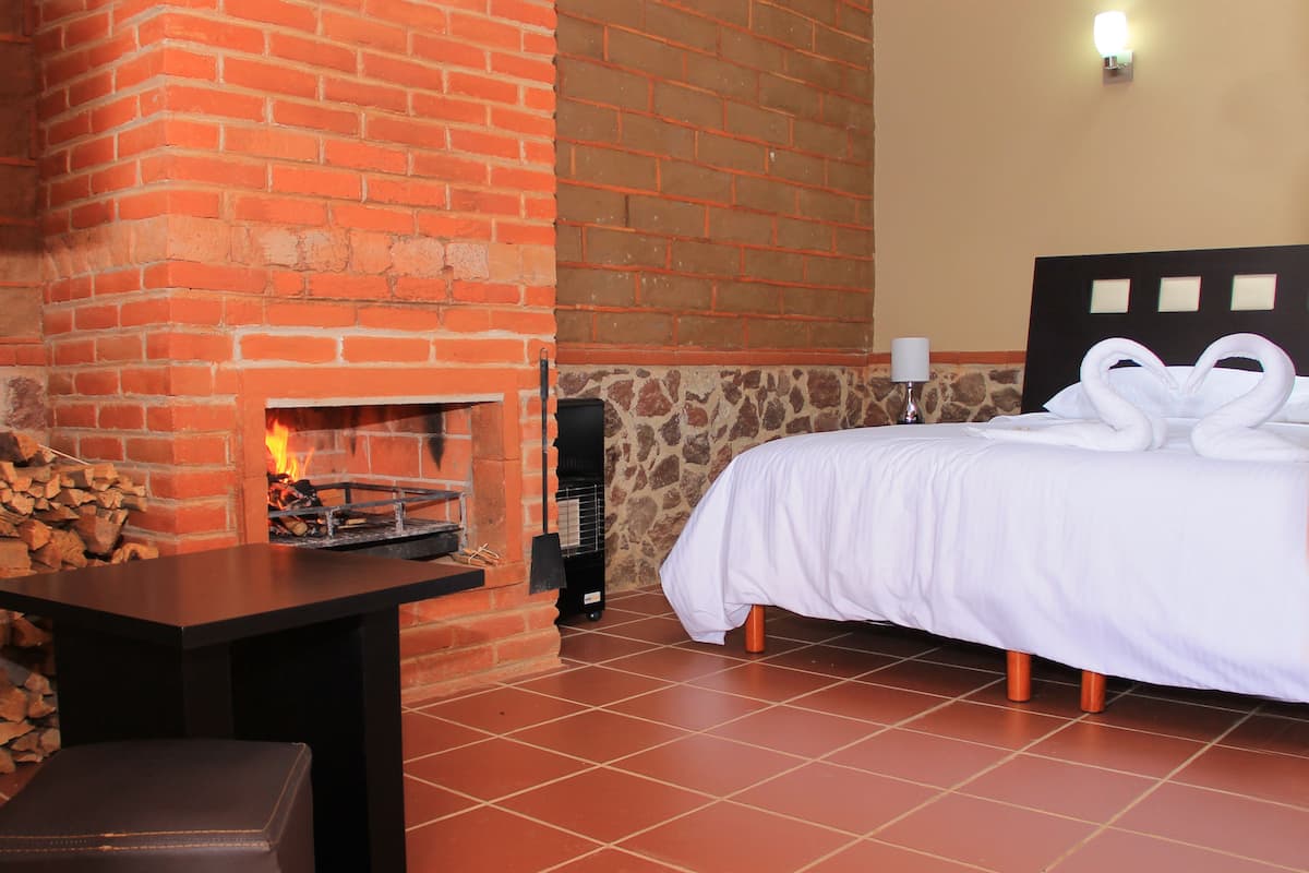 Une chambre d’hôtel avec une cheminée en briques, un lit avec une literie blanche et une table avec une chaise.