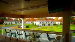 A covered outdoor area with wooden flooring and black chairs, overlooking a residential area with houses and a green lawn. - The Loon (Gaylord)