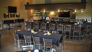 A bar area with multiple tables and chairs, a television screen, and a variety of bottles and glasses on shelves. - The Loon (Gaylord)