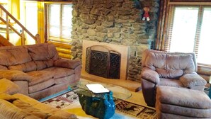 A cozy living room with stone walls, a fireplace, and plush furniture. - The Ridge (Gaylord)