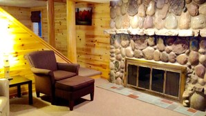 A cozy room with a stone fireplace, a wooden staircase, and a comfortable chair. - The Ridge (Gaylord)