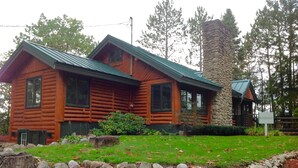 A log cabin with a stone chimney, surrounded by a well-maintained lawn and a stone border. - The Ridge (Gaylord)