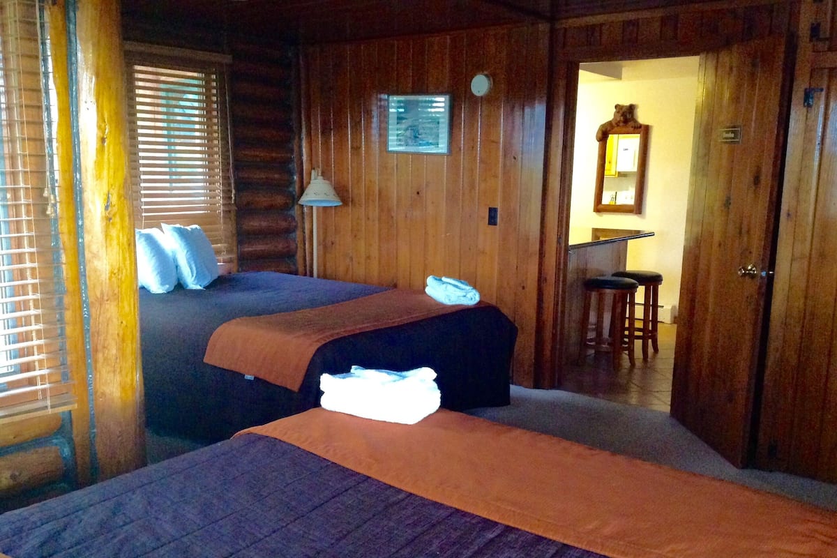 A log cabin room with two beds, a wooden wall, a small desk, and a mirror.