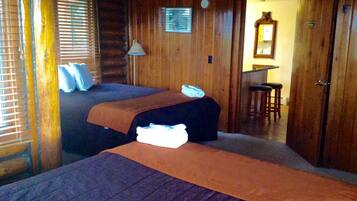 A log cabin room with two beds, a wooden wall, a small desk, and a mirror.