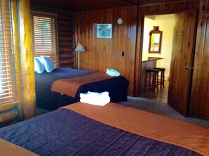 A log cabin room with two beds, a wooden wall, a small desk, and a mirror.