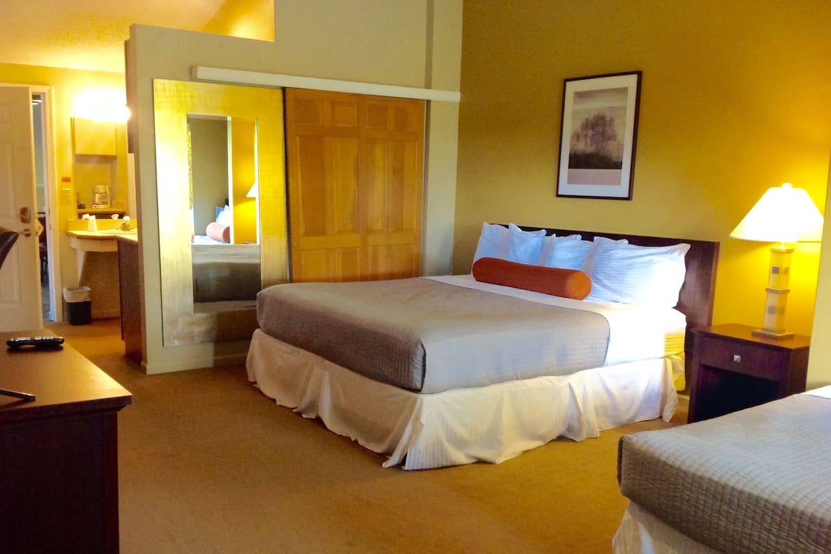 A hotel room with a bed, bedside table, lamp, and a bathroom visible through an open door.