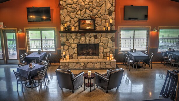 A restaurant with a stone fireplace, multiple tables and chairs, and large windows. - The Ridge (Gaylord)